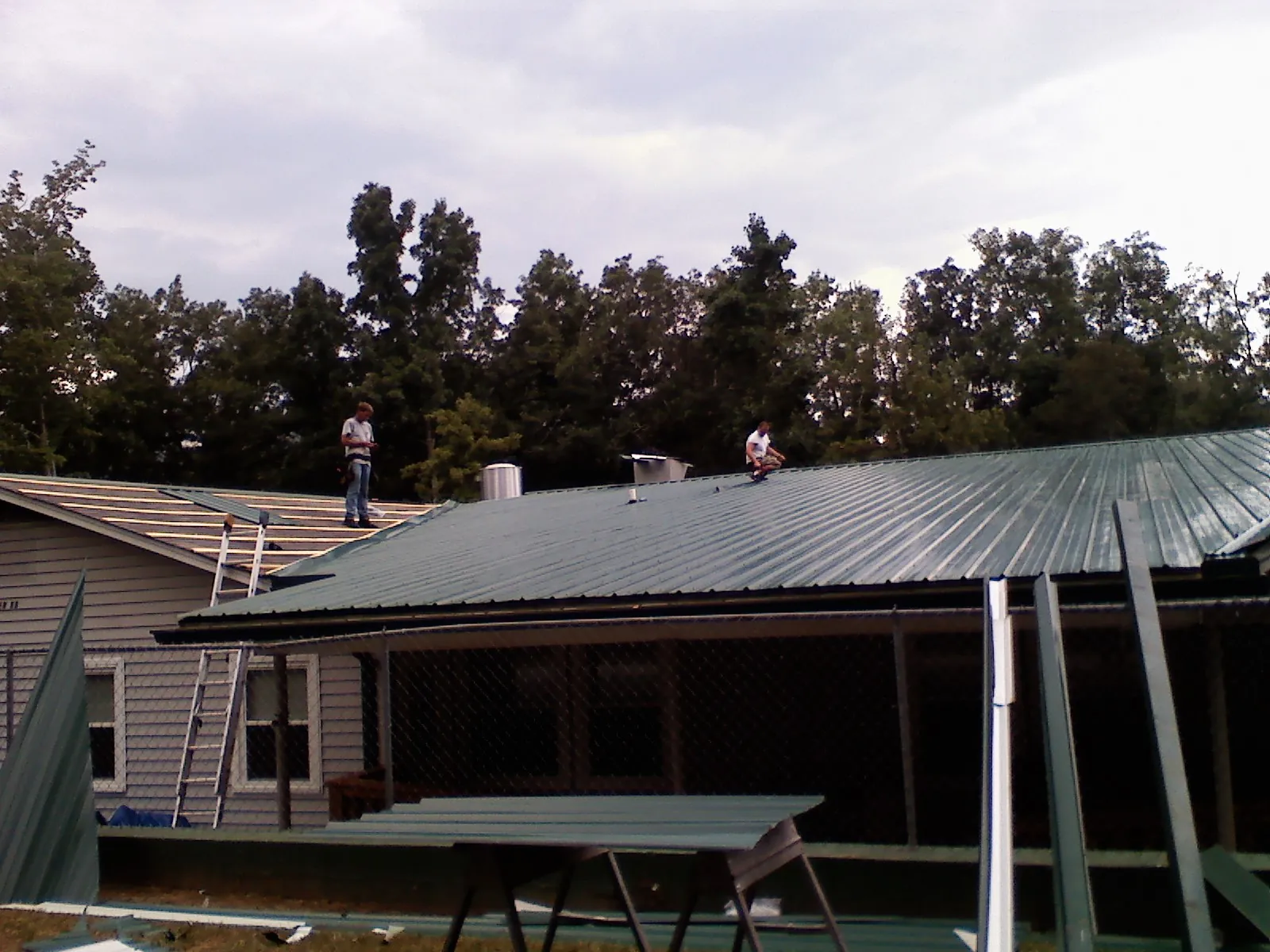Two roofers installing green metal panels above a covered porch in Jacksonville